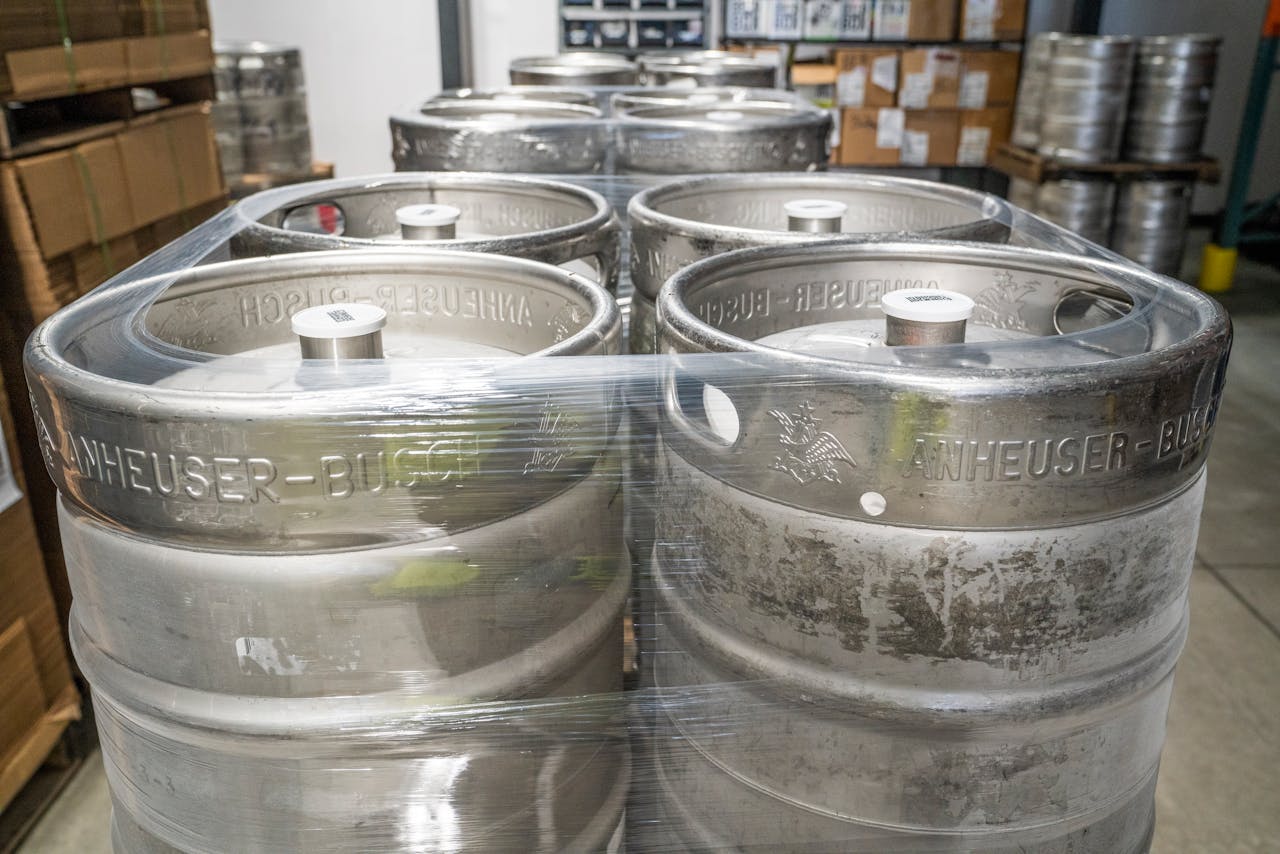 Metal beer kegs stacked and wrapped in plastic in a brewery warehouse, ready for distribution.